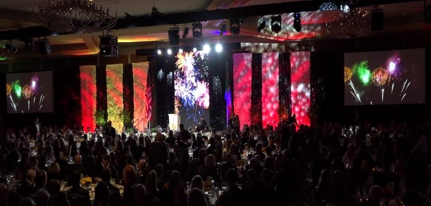 Gala main stage with fireworks projection across full-height screens and a seated audience