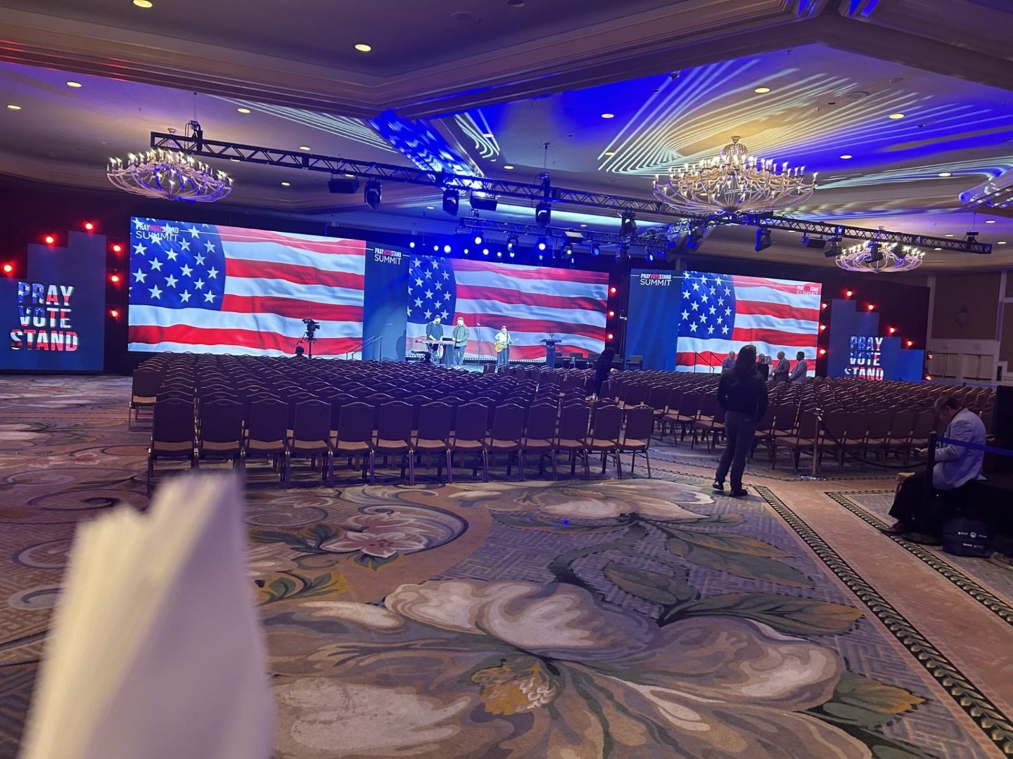 Corporate summit ballroom set with three American-flag stage screens and rows of chairs