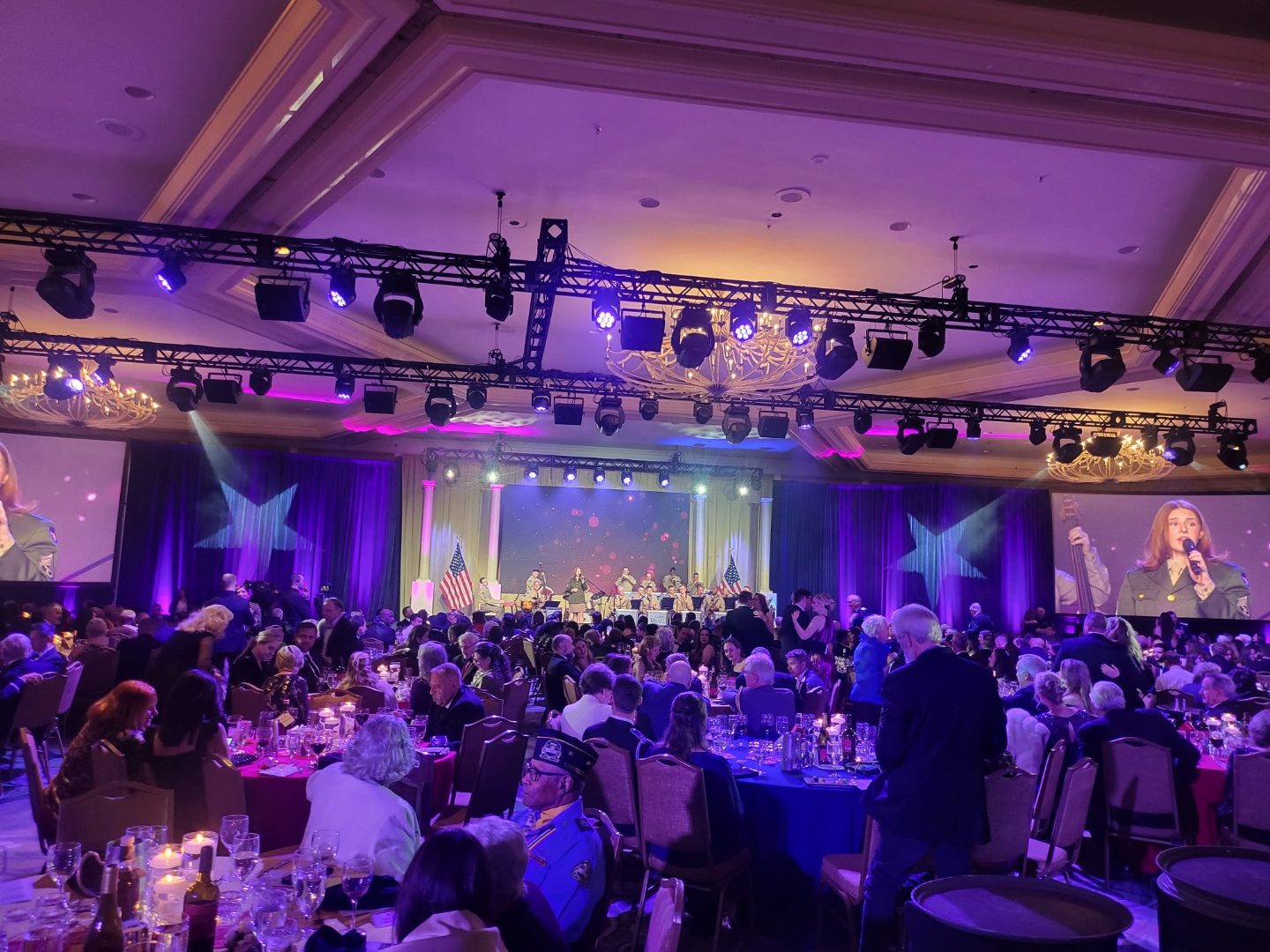 Veterans gala in a grand ballroom with a military honor guard on stage and candlelit dinner tables
