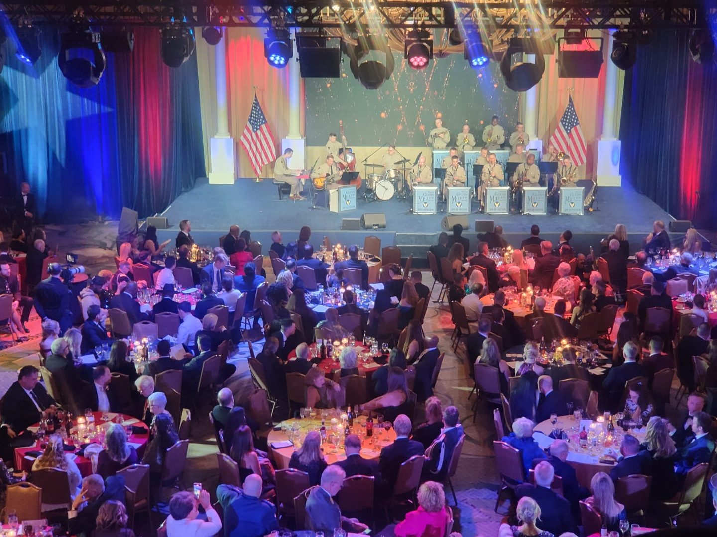 Big band on stage flanked by American flags with a candlelit gala audience below
