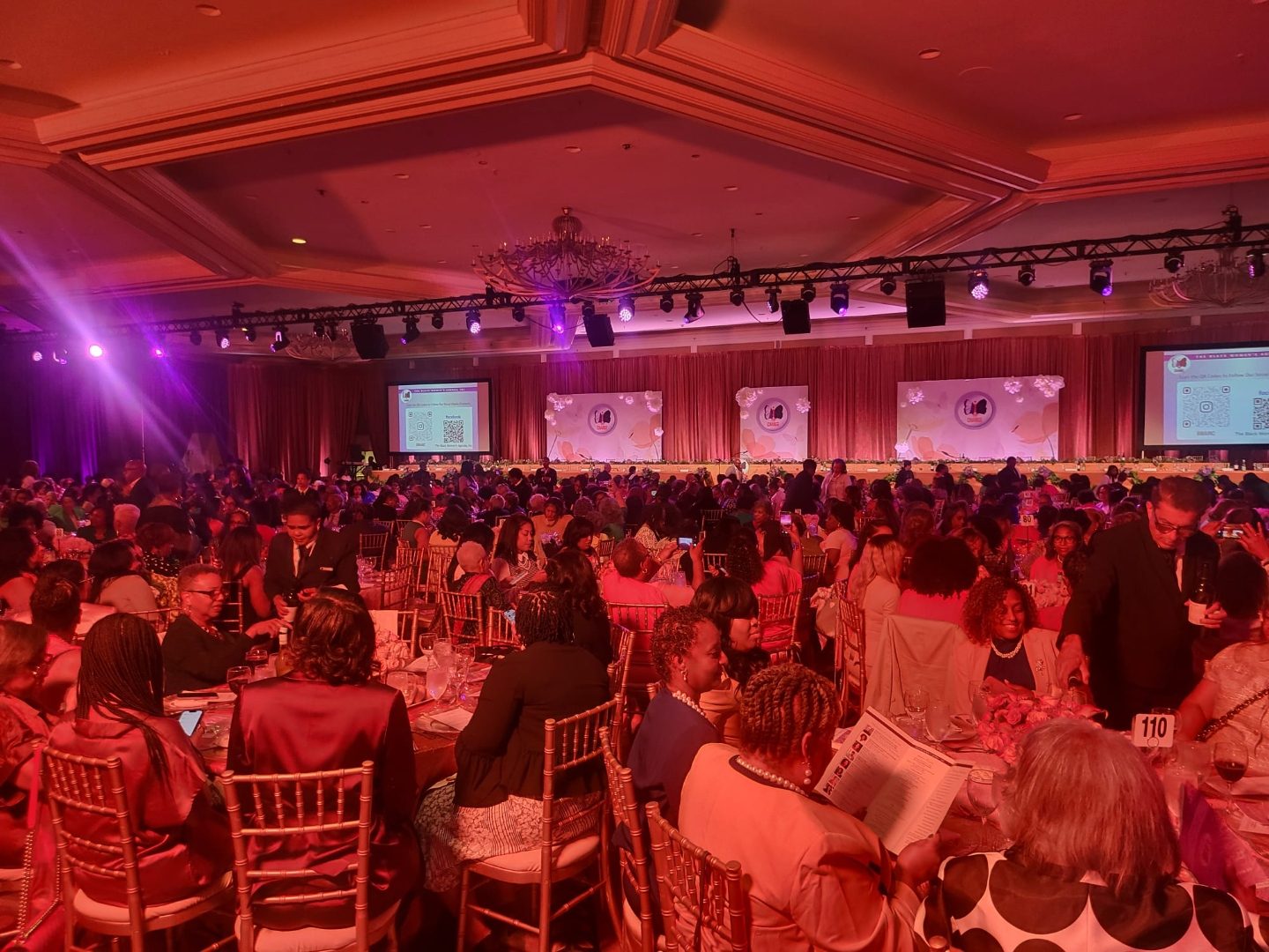 Women's leadership gala in a rose-lit ballroom with round dinner tables and stage screens