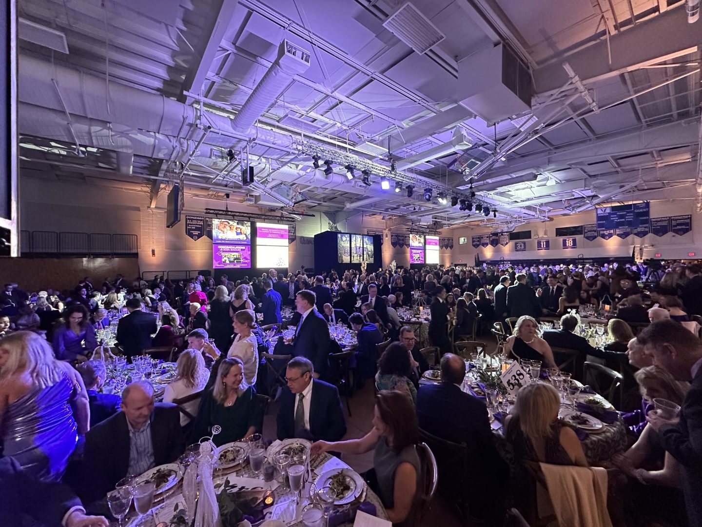 Nonprofit gala reception in a large venue with candlelit round tables and violet stage lighting