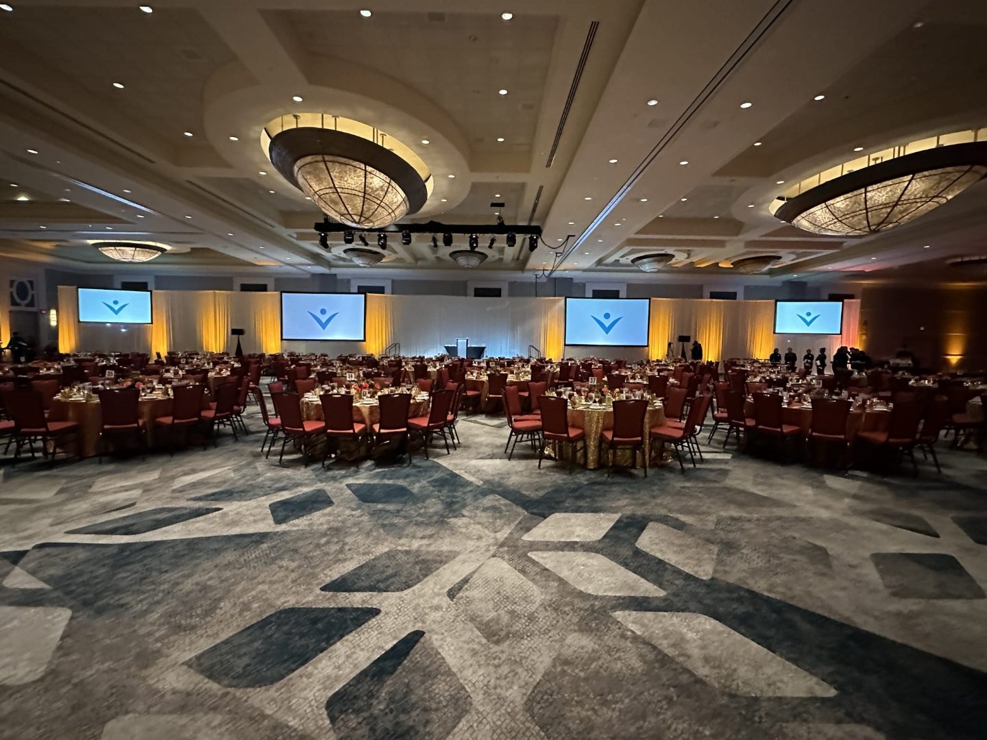 Grand ballroom set for a nonprofit dinner with warm uplighting and round tables